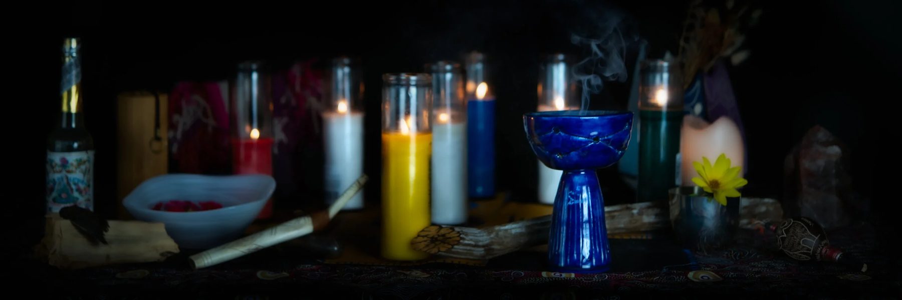 A blue ceramic copalero with rising smoke beside candles on a ceremony table