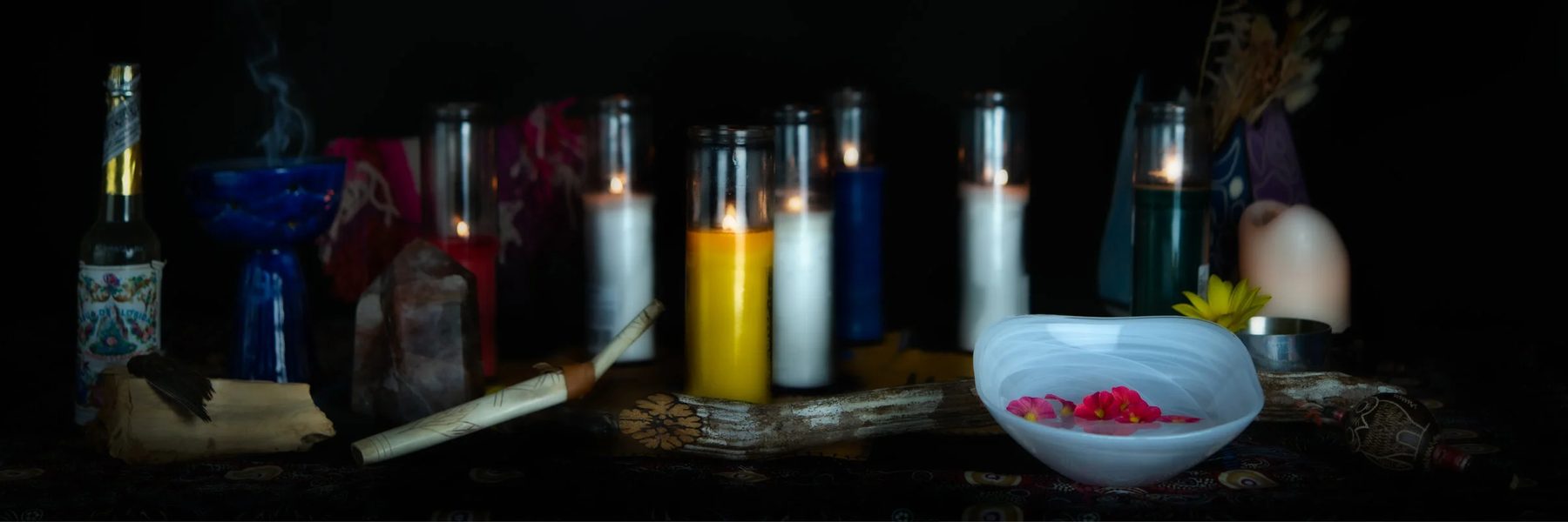 A white glass bowl with pink flowers beside candles