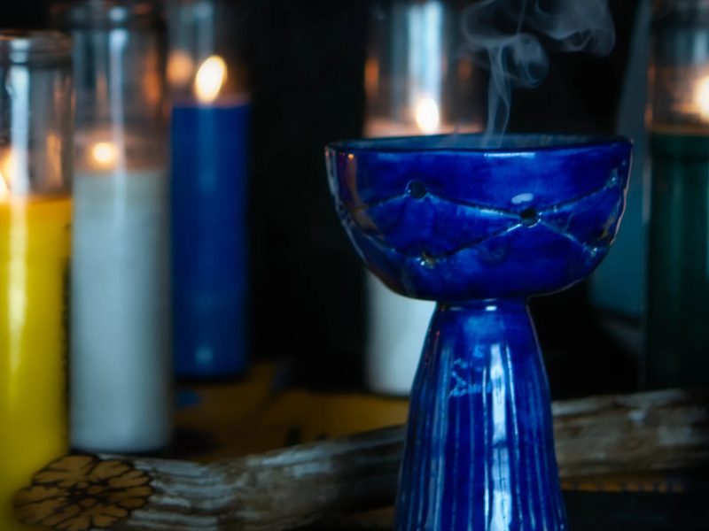 A blue ceramic copalero with rising smoke beside candles