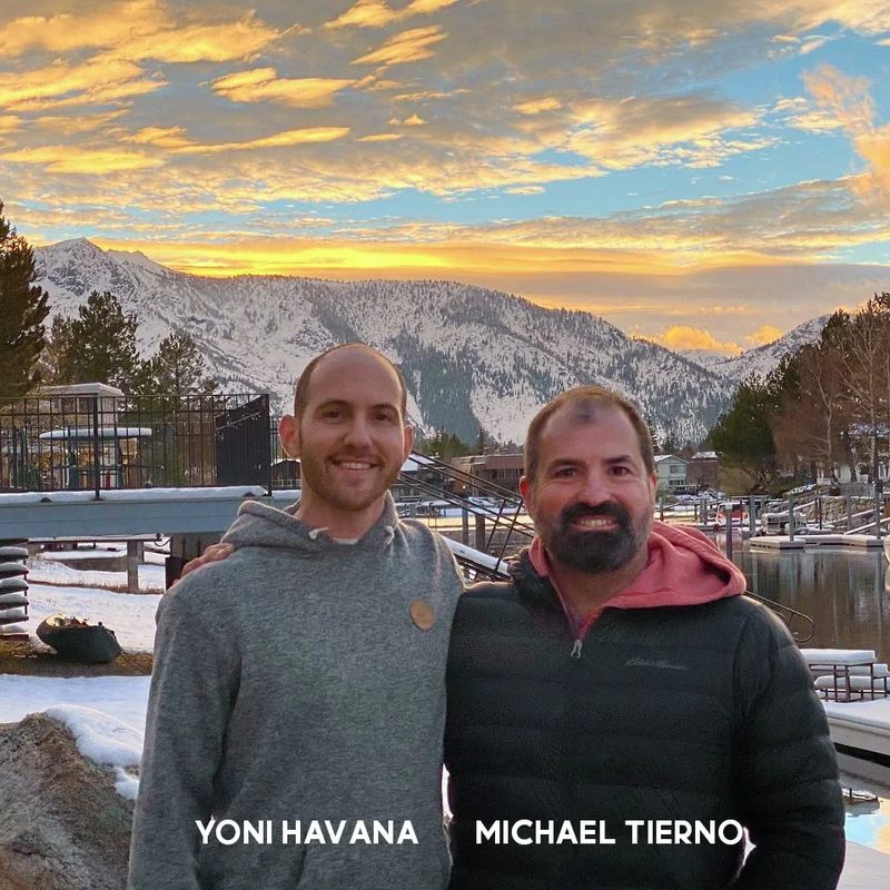 Two men at a marina at sunset with snow-covered mountains behind