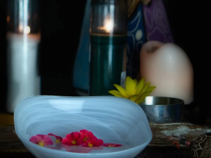 A white glass bowl with pink flowers beside candles